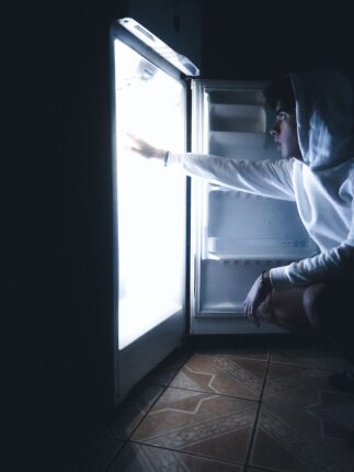 a person in a hoodie reaching into an open refrigerator