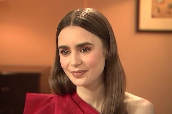 Lily Collins w naturalnej scenerii planu filmowego, nawiązująca kontakt wzrokowy z widzem, uchwycona w autentycznym momencie pracy.
